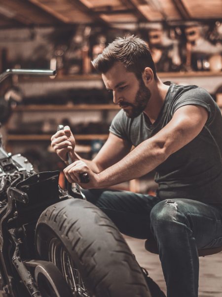 This bike will be perfect. This bike will be perfect. Confident young man repairing motorcycle in repair shop